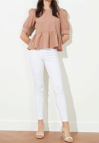 Top peplum in tessuto rosa pallido, con maniche a palloncino e orlo svasato, abbinato a jeans bianchi a vestibilità slim e sandali con tacco.