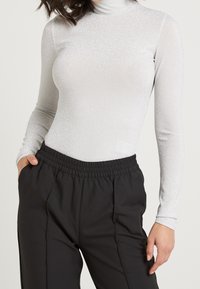 Silberner Langarm-Turtleneck mit schimmernder Textur, kombiniert mit lockeren schwarzen Hosen mit elastischem Bund und Seitentaschen.