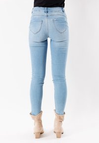 Jeans ajustados de color azul claro con una cintura de altura media, bolsillos traseros y una textura suave, combinados con botas de tobillo beige.