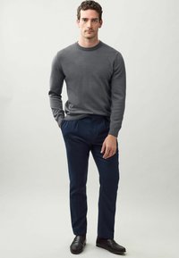 Grauer Strickpullover mit Rundhalsausschnitt, kombiniert mit dunkelblauen maßgeschneiderten Hosen. Das Outfit zeichnet sich durch eine glatte Textur und eine taillierte Form aus.