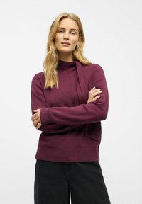 Bordeaux pullover sweater med høj hals, lange ærmer og ribbede manchetter. Fremstillet af blødt materiale, har den en sidesløjfe-detalje og en afslappet pasform.