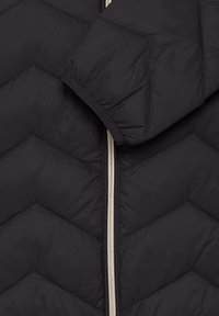 Črna prešita jakna s Chevron vzorcem, opremljena s srebrnim zadrgo in elastičnimi manšetami za prilegajoč se dizajn. Mehka, lahka tkanina.