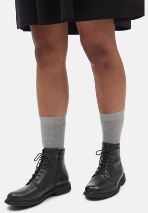 Black leather ankle boots with laces and side zipper. Paired with gray ribbed socks. Smooth texture, rounded toe, and flat sole.