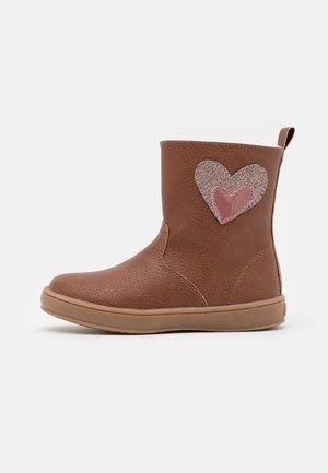 Brun læderbørnestøvle med to lagdelte hjerte-patches på siden, et glitrende og et ensfarvet pink, samt en træk-flap bagpå.