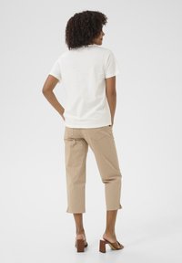White cotton t-shirt, short sleeves, relaxed fit; paired with beige cropped pants and brown block-heeled sandals. Simple, casual style.