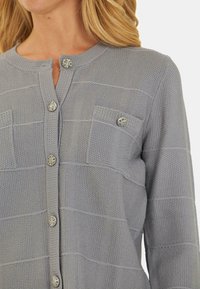 Cardigan grigio lavorato a maglia con un motivo testurizzato, due tasche frontali e bottoni tondi in tonalità argento lungo la patta anteriore.