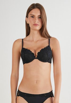 Soutien-gorge en dentelle noire avec bonnets rembourrés, bords festonnés et bretelles ajustables, associé à un bas de bikini avec des bordures en dentelle assorties.