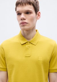 Polo jaune en tissu texturé, avec col classique, trois boutons et un petit logo embossé sur la poitrine.