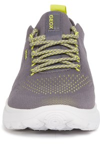 Zapatillas de punto gris con acentos amarillos y detalles texturizados. Presentan una suela blanca redonda y un sistema de cordones prominente en la parte frontal.