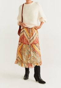 Pull : crème, tricot texturé. Jupe : mi-longue, motif paisley multicolore avec volants. Chaussures : bottes de cow-boy noires, à bout pointu. Sac à main : marron.