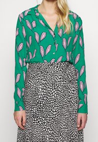 Blusa verde con motivo a foglie, con accenti rosa, abbinata a una gonna nera decorata con cuori bianchi; entrambi in tessuto morbido e fluido.