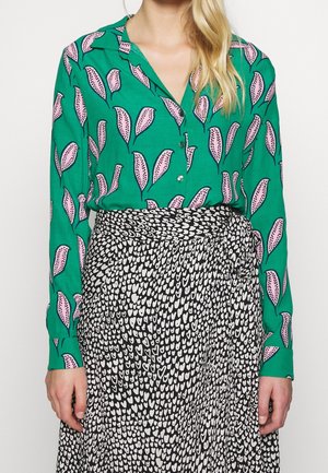 Blouse verte avec motif de feuilles, ornée d'accents roses, associée à une jupe noire recouverte de cœurs blancs ; les deux en tissu doux et fluide.