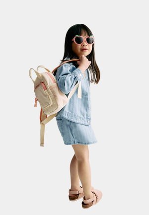 Lys beige rygsæk med lyserøde elementer, denimjakke og nederdel. Pigen har hjerteformede solbriller og lyserøde sko på. Enkel, afslappet design.