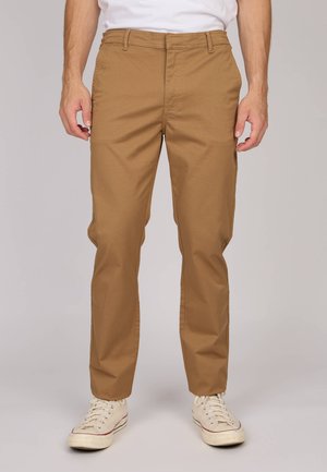 Chino kaki avec une coupe droite, en mélange de coton doux, avec passants de ceinture et deux poches avant. Porté avec des baskets blanches.
