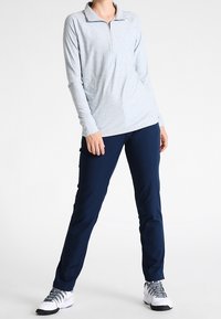 Ljust grå långärmad topp med zippered hals, i kombination med mörkblå träningsbyxor. Båda är tillverkade av stretchigt, slätt tyg.