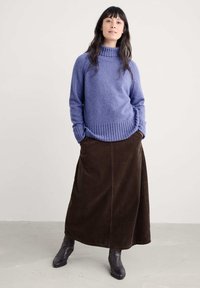 Overmaatse lavendelkleurige coltrui met ribbelzoom, gecombineerd met een lange bruine corduroy rok, aangevuld met zwarte enkellaarsjes.