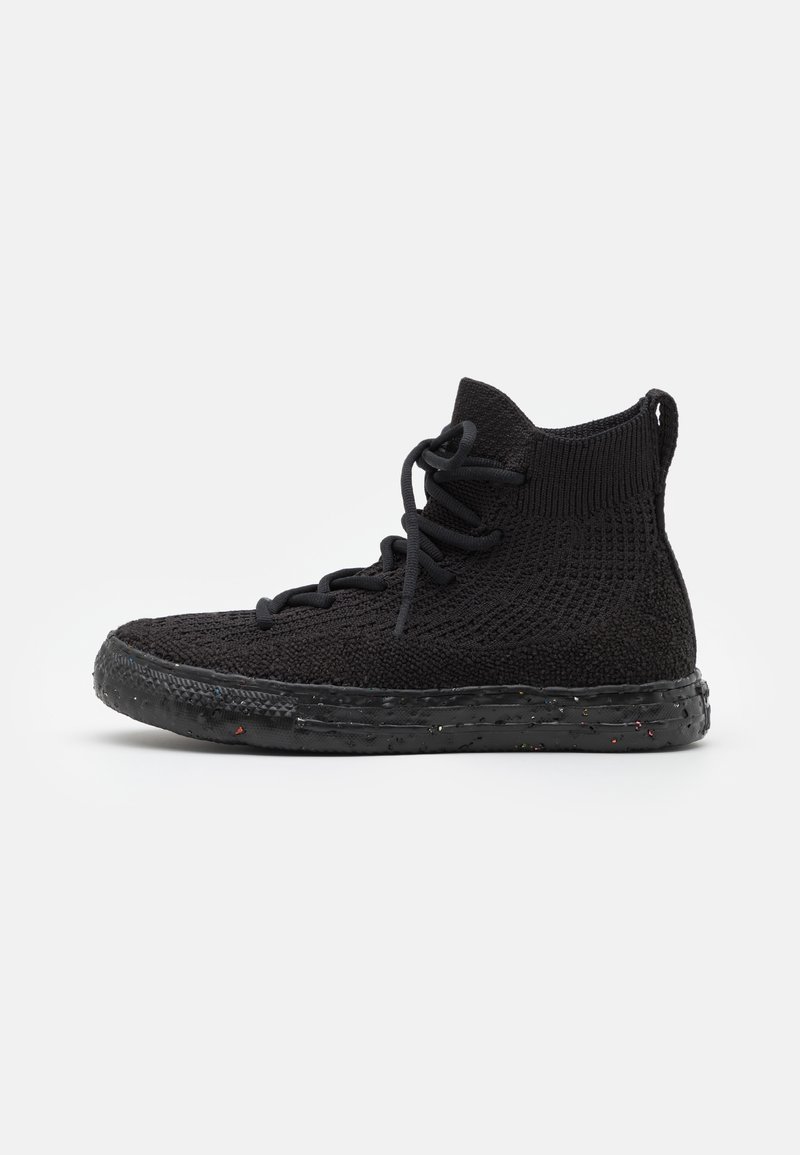 Baskets montantes noires en tissu tricoté, fermeture à lacets et semelle texturée avec de petites taches colorées, vues de côté sur fond blanc.