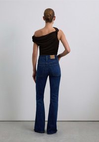 Top nero scollato con tessuto drappeggiato; jeans flare in denim blu a vita alta con una pattina in pelle sul retro della vita.