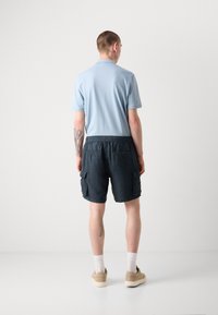 Polo shirt bleu clair, shorts cargo foncés avec poches latérales, baskets beiges et chaussettes blanches. Design minimaliste avec une coupe décontractée.