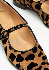 Zapatos de ante con estampado de leopardo, con una correa y detalles en charol negro, puntera redonda y tacón bajo. Suela plana y forro interior suave.