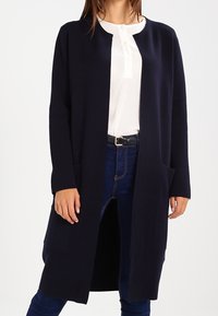 Marineblauer langer Cardigan aus weichem Stoff mit offenem Vorderteil, zwei seitlichen Taschen und rundem Ausschnitt. Er hat lange Ärmel und einen lockeren Schnitt.