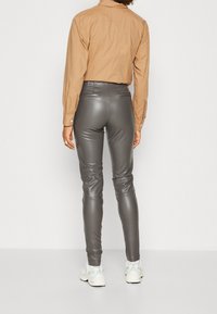 Grå faux läderbyxor med slim fit och slät yta, tillsammans med en ljusbrun skjorta med knappar. Synliga bakfickor och anklar.