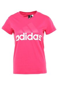 Różowa bawełniana koszulka z okrągłym dekoltem, krótkimi rękawami oraz dużym białym logo "adidas" z trzema ukośnymi paskami.