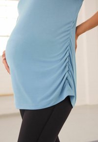 Világoskék kismama felső, texturált oldalsó ráncolással, fekete leggings-el párosítva. Simaságot és kényelmet biztosító laza szabású anyag.