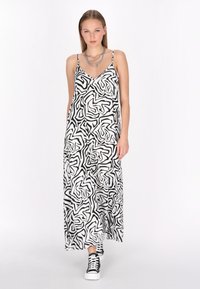 Rochie maxi în alb și negru cu model abstract. Material ușor, decolteu în V, bretele ajustabile, asortată cu adidași negri.