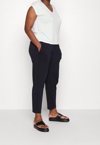 Witte V-hals T-shirt, marineblauwe tapershorts met voorzakken, en zwarte instapsandalen. Zachte stof, relaxte pasvorm en minimalistisch ontwerp.