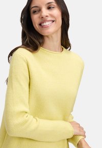Żółty sweter z dzianiny o prążkowanej fakturze, okrągłym dekolcie i długich rękawach, z miękkiego materiału i luźnym krojem.