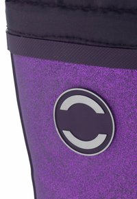 Purppuranen astia, jossa on teksturoitu pinta, musta yläosa ja pyöreä hopeinen logo. Tasainen pinta, jossa on heijastava kiilto.