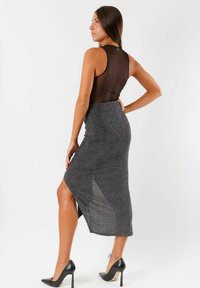 Body negro transparente combinado con una falda midi gris texturizada con una abertura lateral, complementado con tacones de aguja negros.
