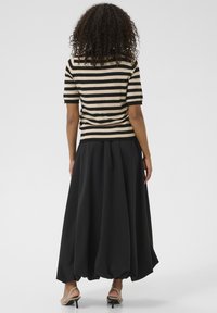 Jupe maxi noire fluide avec un ourlet froncé et une taille élastique, associée à un haut à rayures à manches courtes en beige et noir.