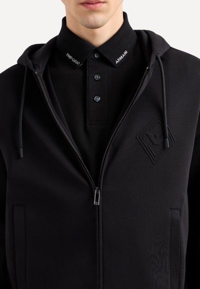 Sweat à zip noir avec une finition texturée, doté d'une capuche, d'un col polo noir contrastant avec boutons et de logos de marque brodés.