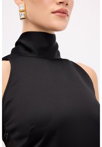 Sort højhalset top lavet af et glat stof. Har store firkantede øreringe med guld og klare ædelsten samt et ærmeløst design.