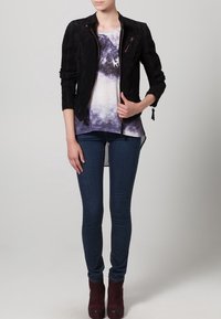 Zwarte suède motorjas met een aansluitend ontwerp, voorzien van een ritssluiting, gecombineerd met een paars tie-dye shirt en donkere denim skinny jeans.