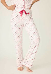 Dvojdílná pyžamová souprava z bílé látky s rozptýlenými růžovými a červenými srdíčky. Vybavena růžovou stuhou, rozšířenými nohavicemi a lemováním.