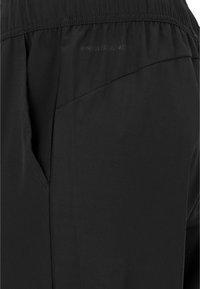 Schwarze Sporthose aus leichtem, glattem Gewebe, mit elastischem Bund und schrägen Seitentaschen sowie minimalem Markenlogo.