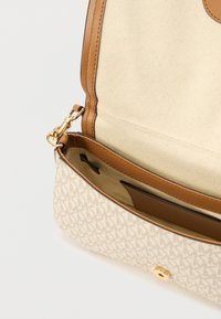 Τσάντα χειρός σε μπεζ με σχέδιο, με δερμάτινες λεπτομέρειες σε καφέ χρώμα, χρυσό κούμπωμα και ανοιχτό καπάκι που αποκαλύπτει εσωτερική θήκη με επένδυση από ύφασμα.