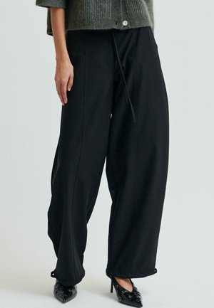 Pantalones de pierna ancha negros hechos de una tela suave, con cintura con cordón, bolsillos laterales profundos y detalles de costura sutiles.