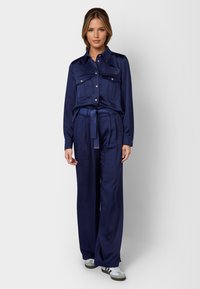 Navy satin two-piece set featuring a button-up shirt with chest pockets and wide-leg trousers with a tie waist. Includes sneakers.