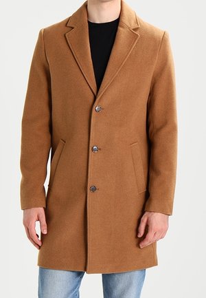 Manteau en laine camel marron pour homme, à simple boutonnage avec revers crantés, trois boutons, poches latérales, porté sur un haut noir et un jean bleu.