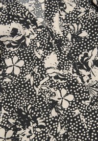 Svart och gräddfärgad tyg med blommönster och prickar, med en mjuk textur och en V-halsdesign.