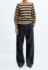 Pull en maille tan avec des rayures noires, associé à un pantalon large à taille haute noir avec des plis. Chaussures fermées marron.