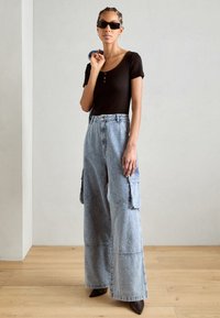 Top negru, ajustat, cu mâneci scurte, asortat cu pantaloni cargo din denim bleumarin, cu picioare largi și buzunare laterale, și pantofi cu toc ascuțit negri.