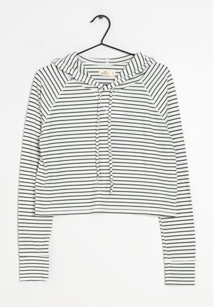 Hvid cropped hættetrøje med tynde sorte vandrette striber og snore, vist på en sort bøjle mod en hvid baggrund.