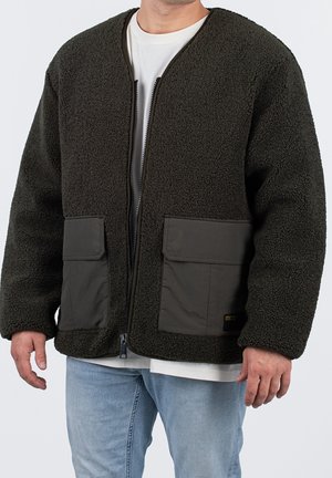 Veste en polaire vert foncé avec une surface texturée, dotée d'une fermeture éclair à l'avant et de deux poches avant, rehaussée par un panneau inférieur gris foncé.