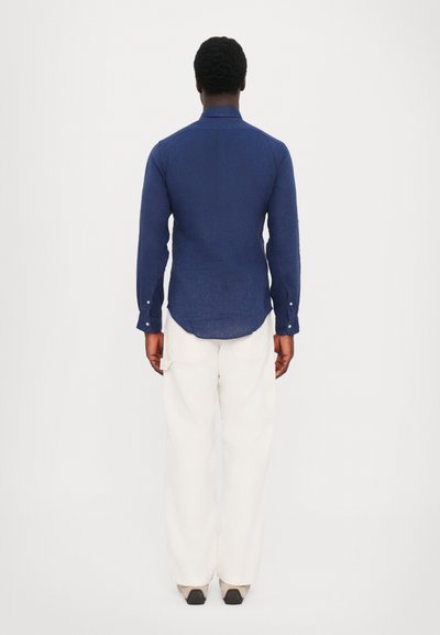 Temno modra srajca z dolgimi rokavi iz teksturirane tkanine, ravnega kroja in s ஷептелами, v kombinaciji s širokimi belimi hlačami.