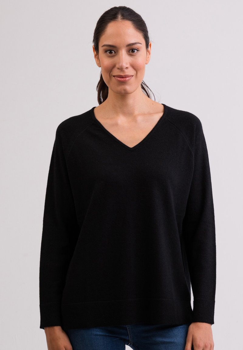 Czarny sweter w serek o miękkiej fakturze, z długimi rękawami raglanowymi i luźnym krojem, noszony na niebieskich dżinsach. Prosty i uniwersalny design.